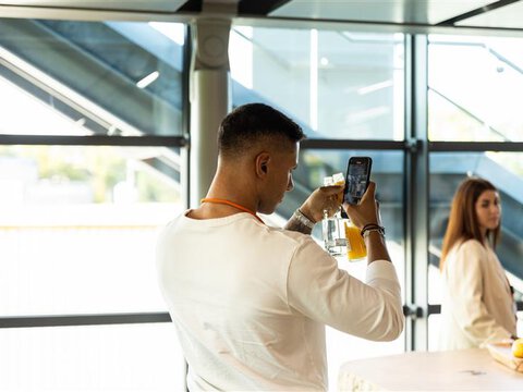 Mann fotografiert Produkt mit Smartphone bei BORA Event in modernem, lichtdurchflutetem Raum.